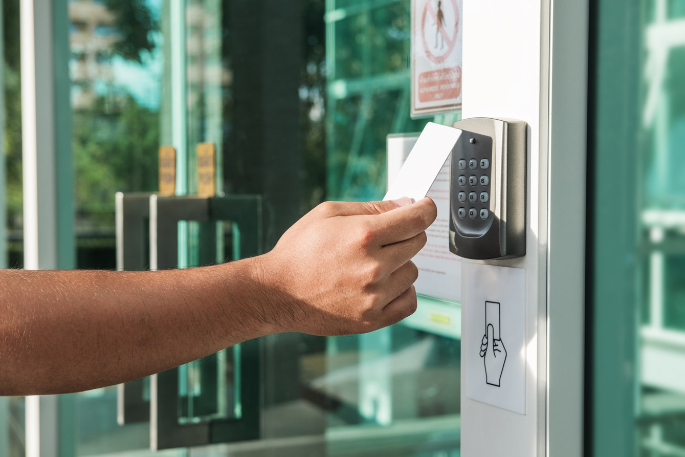 An unseen person uses a keycard on an exterior door access control panel.